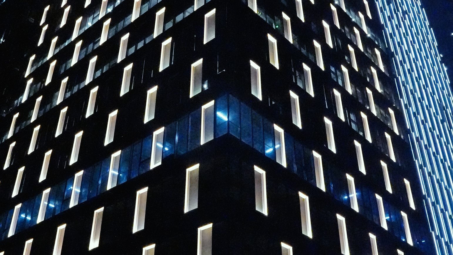 A tall office building at night with rows of glowing vertical window slots
